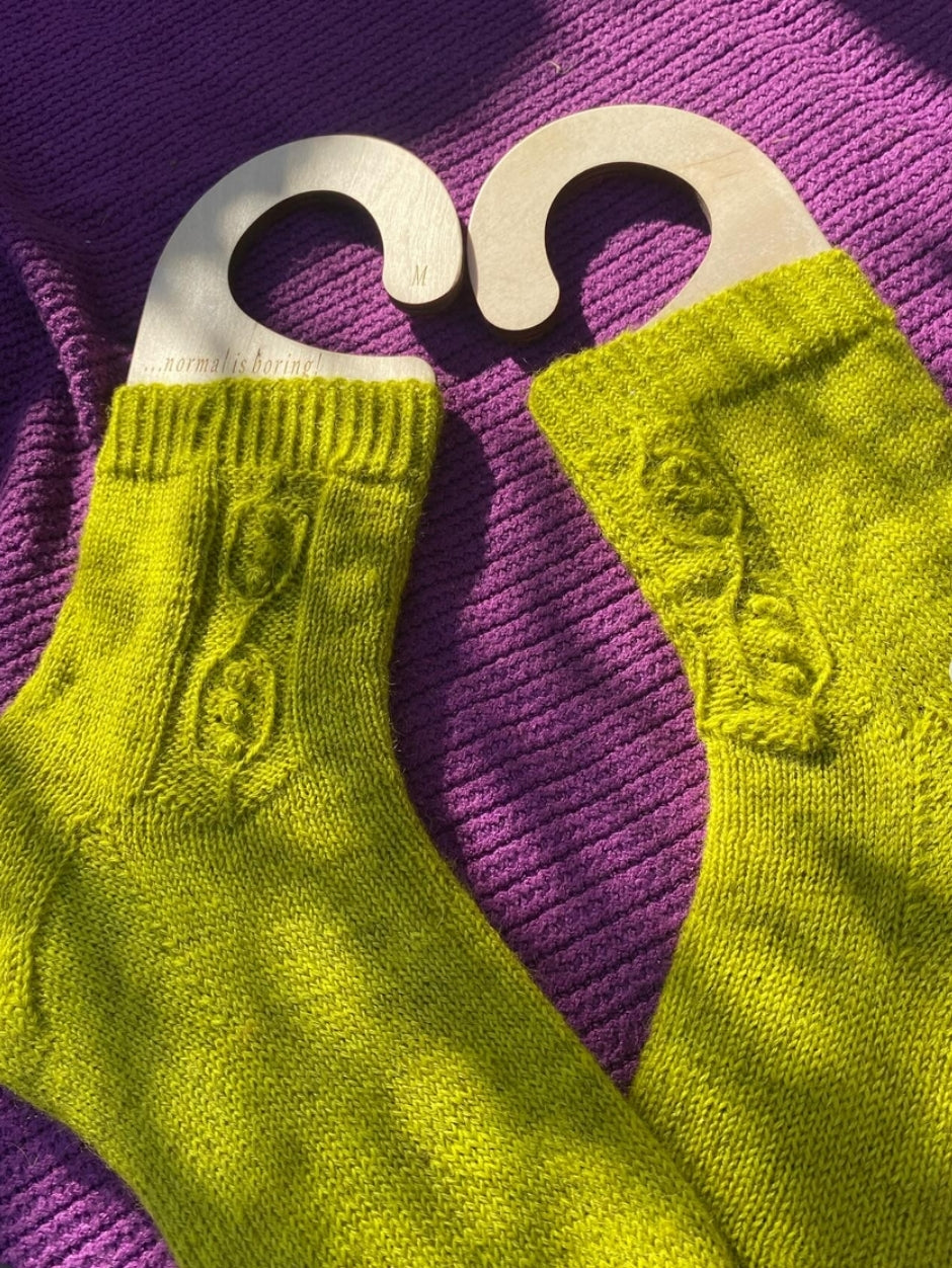 Bright yellow-green socks featuring a peapod design on a sock-blocker that says 'Normal is boring!'