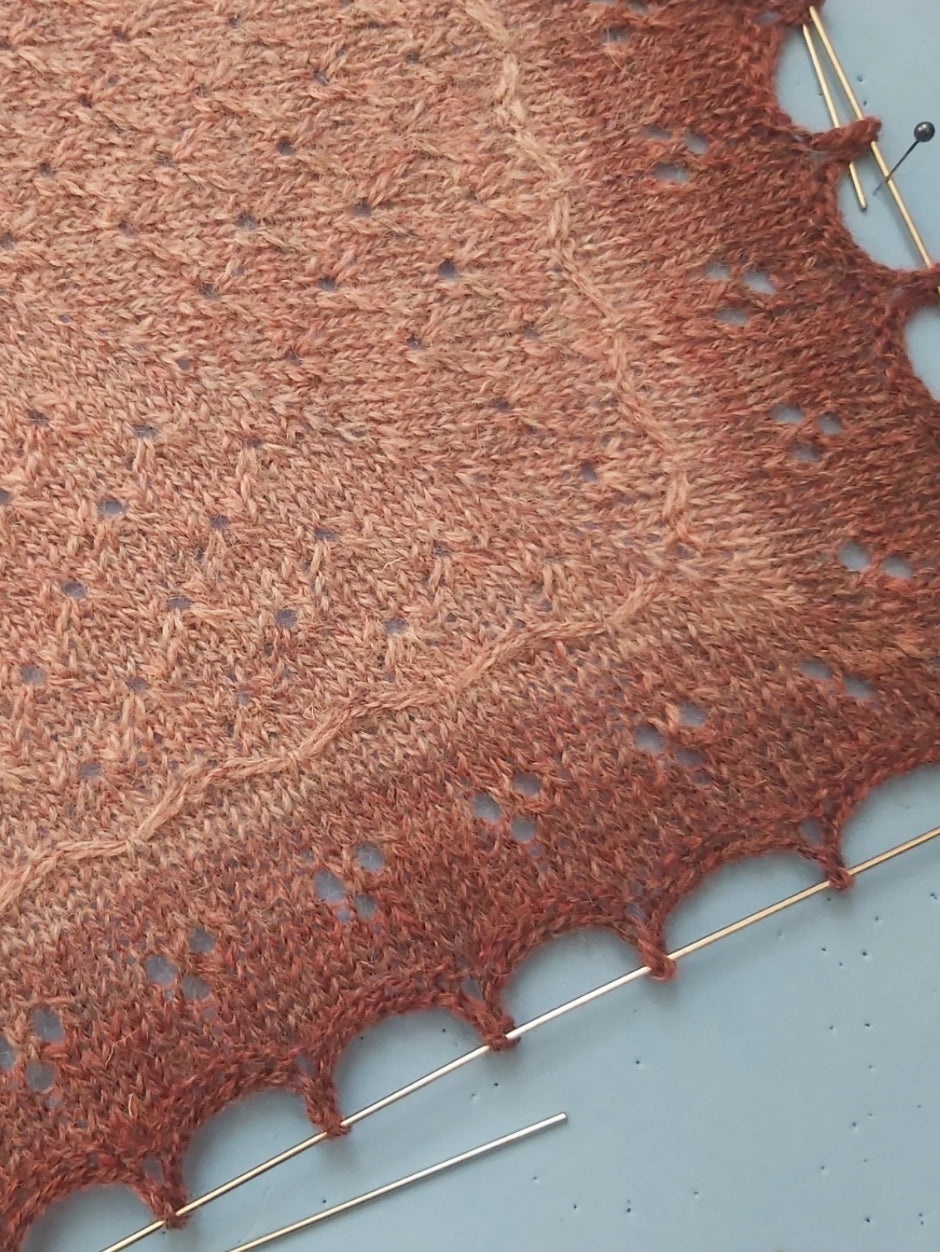 A knitted shawl in peachy tones with a delicate eyelet design.