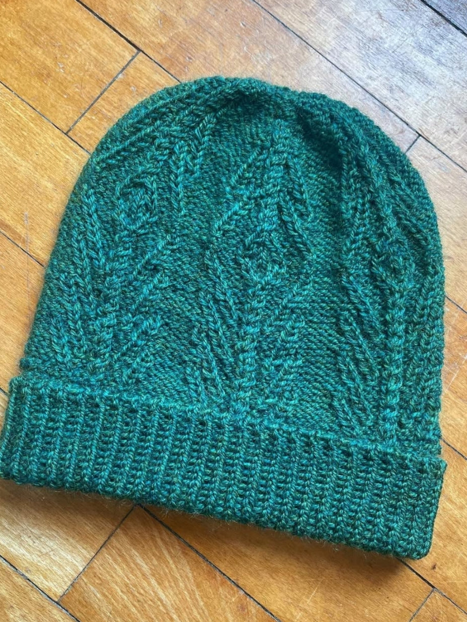 A teal knitted beanie on a wooden floor. 