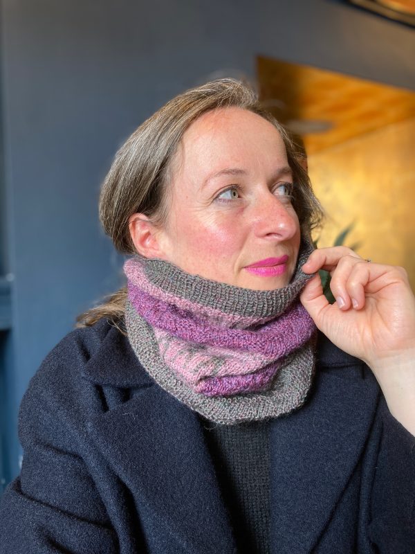 A person is wearing a pink, purple and grey cowl over a navy coat