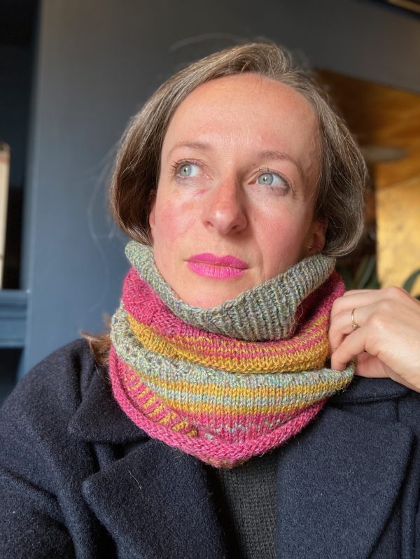 A person is wearing a pink, yellow and green version of a knitted cowl