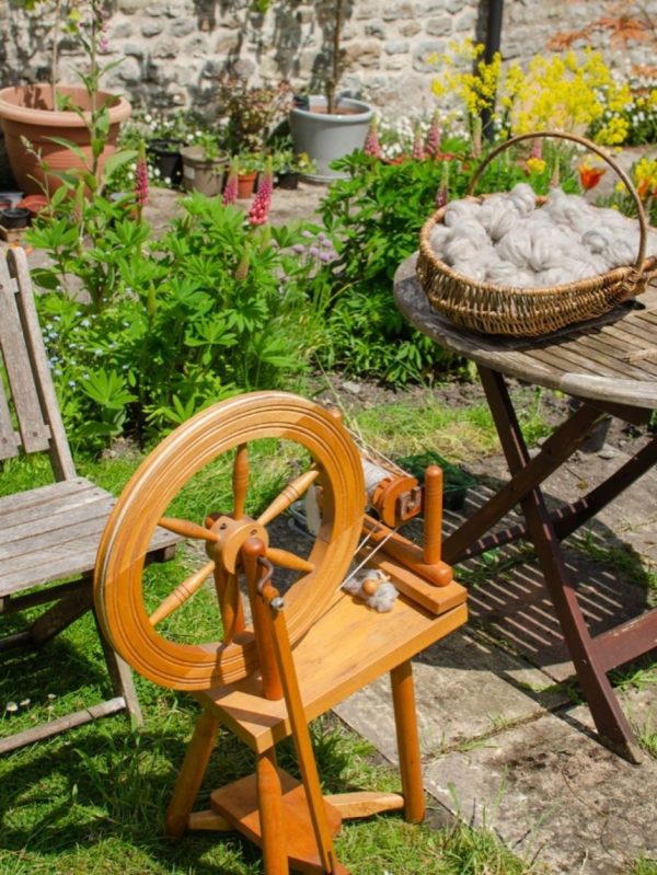 A spinning wheel in a garden with a basket of fibre ready to spin.