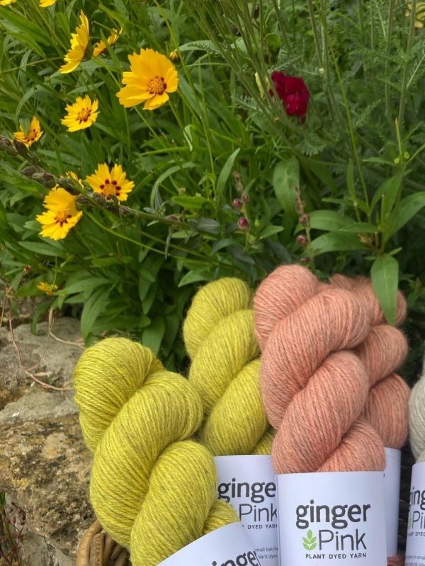 A collection of yellow and peach skeins of yarn among flowers.